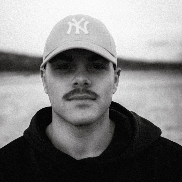 a man with a baseball cap on standing in front of a body of water