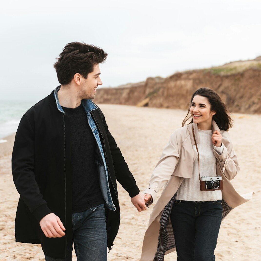 a man and woman walking on the beach holding hands