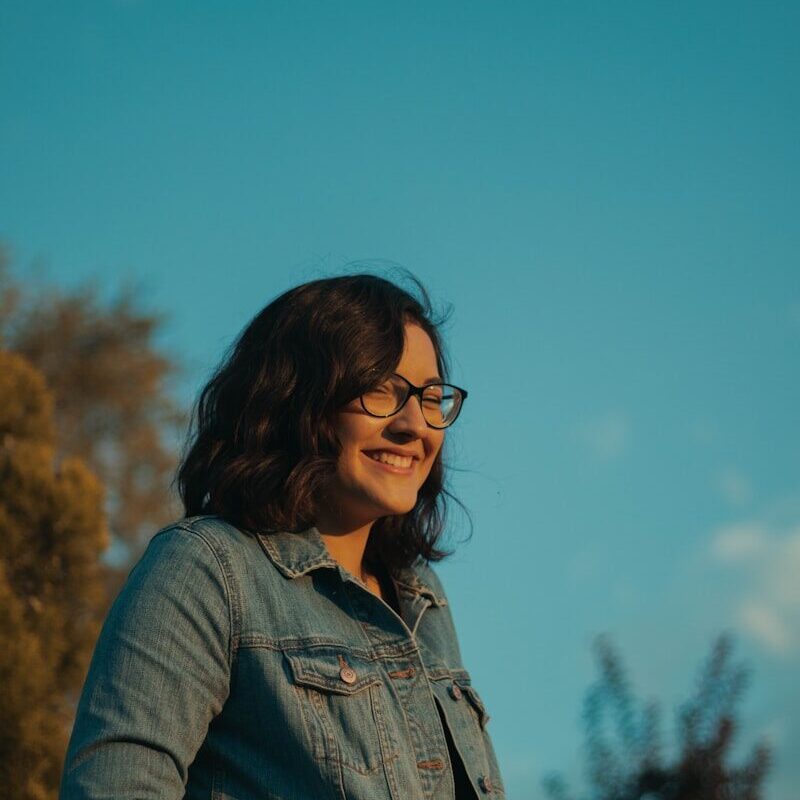 woman wearing blue denim jacket and eyeglasses standing and laughing
